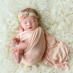 Adorable baby girl swaddled in pink with a floral headband