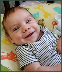 Baby boy smiling, propped up on a pillow