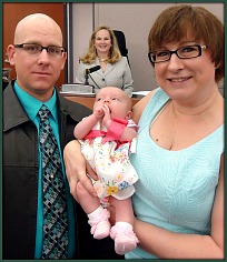 Adoptive parents holding baby with judge in background