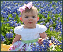 Baby girl in an Easter dress posed by a field of Bluebonnets