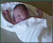 Newborn baby Zach sleeps happily, swaddled in a blanket