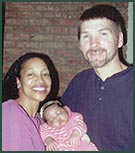 Biracial couple holding newly adopted baby in striped onesie