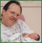 Smiling adoptive dad holds his baby in the hospital