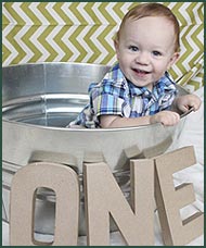 Smiling baby boy in tub with the letters O, N, and E