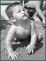 Black and white photo of a baby boy crawling at a beach