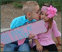 Boy kisses his sister while holding a sign