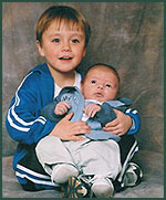Three year old in track suit holding new baby brother up for photo
