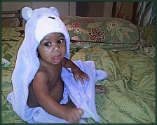 Black baby boy in a hooded towel on a bed