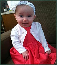 Happy baby girl in a headband, dress, and cardigan