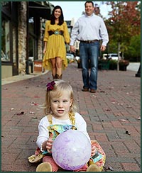 Toddler girl with a ball as her parents walk toward her