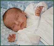 Tiny baby in white dress sleeping with hands up