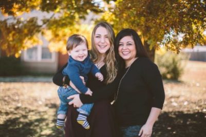 two women and a young one year old boy pose together for the camera outside