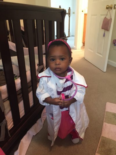 Toddler girl dressed as doctor in front of crib
