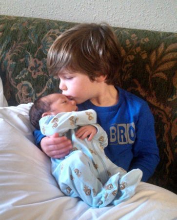 young boy holds his newly adopted sibling and give them a kiss
