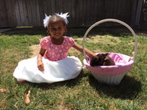 Little girl dressed up, posed outside by a bunny in a basket
