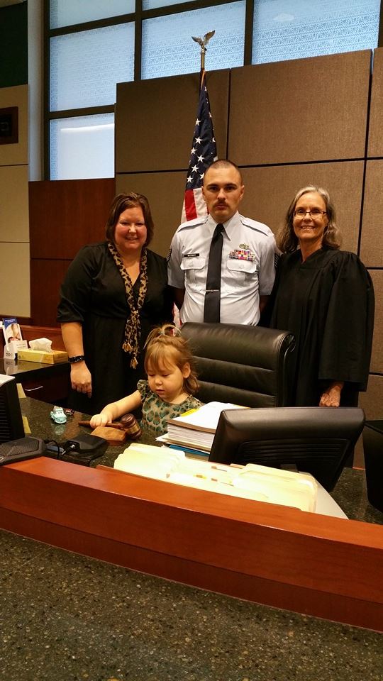 A little girl playing with a gavel at the courtroom while her parents pose