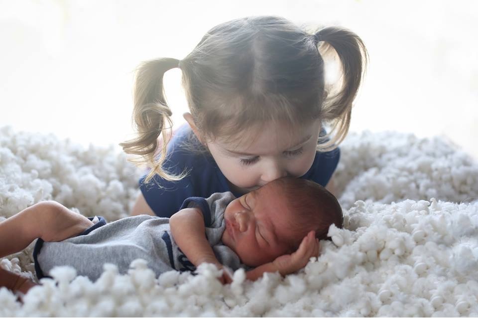 Newborn baby Malachi sleeps while his big sister kisses him