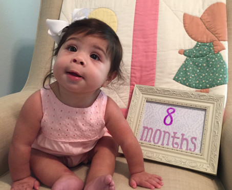 Baby girl poses next to a sign reading 8 months