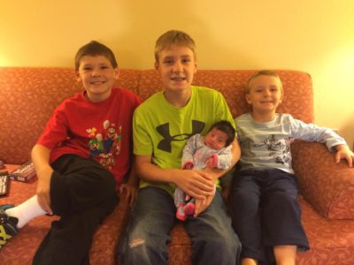 Three brothers hold their newly adopted sibling and smile