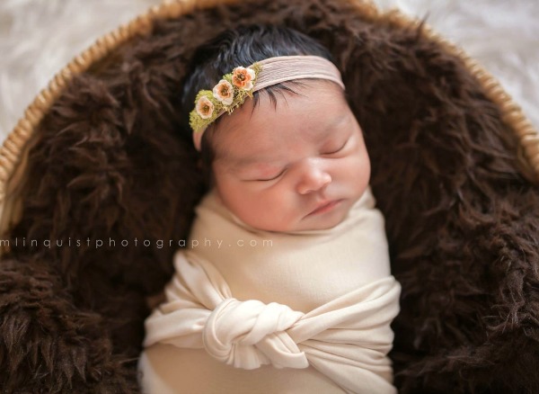 Swaddled baby with headband lays in fur lined cradle
