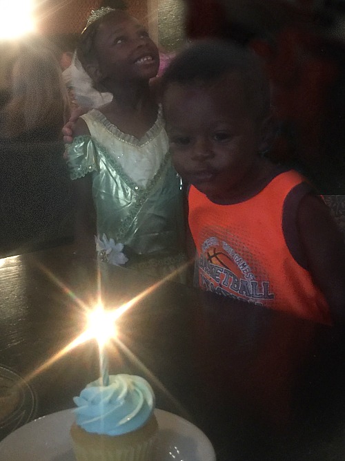 Little boy about to blow out his birthday candle as his sister looks on