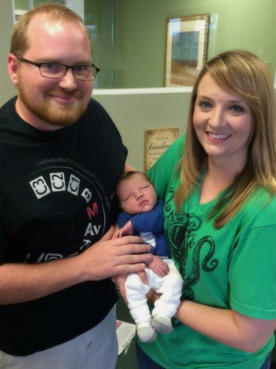 Adoptive couple holding new baby with blue shirt, white pants and gray booties