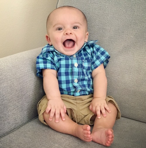 Happy baby in plaid shirt on couch with big smiles