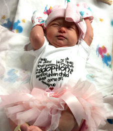 baby with adoption onesie on and pink tutu