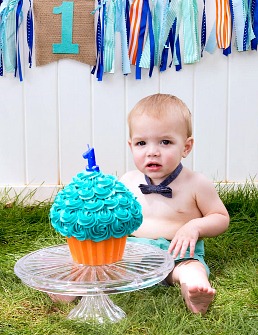 Baby with bowtie and no shirt in front of one year old cupcake cake