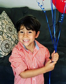 young boy with a bunch of balloons smiles at camera