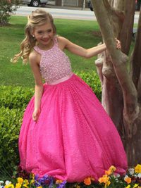 little girl in pageant dress poses by a tree