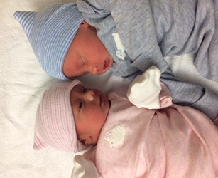 boy and girl twin infants wrapped in blue and pink blankets face each other