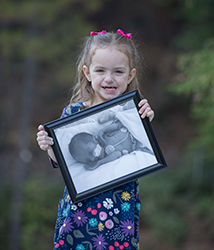 Little girl holds a photo of herself in NICU as a newborn