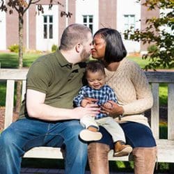 Kissing couple sitting on a bench holding their son together