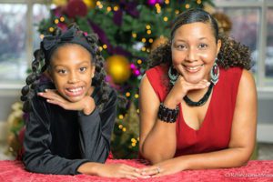 A black adoptive mom poses by the Christmas tree with her daughter