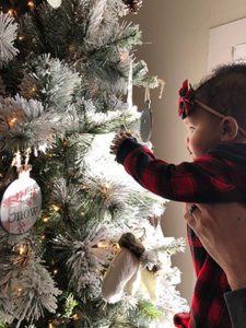 Baby girl being held up next to a Christmas tree