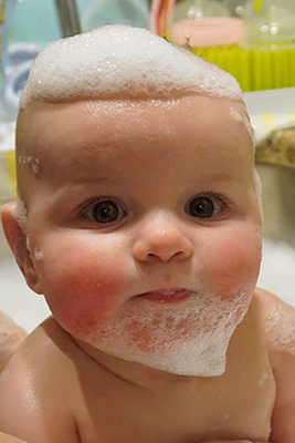 Baby in bath with bubbles on head and chin