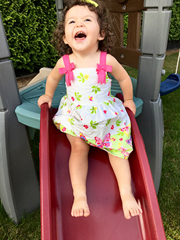 Toddler with summer dress sliding down small backyard slide