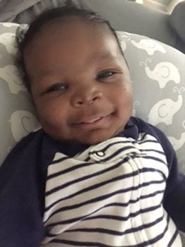 8 week old boy smiling and laying on whale covered pillow