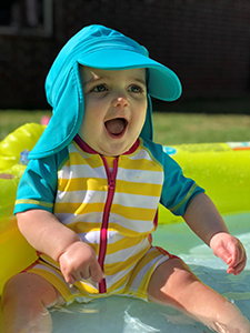 Baby with sun hat siting in shallow water