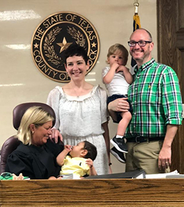 Judge holding adopted baby in court with family