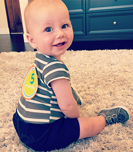Baby boy sitting up with a 5 month sticker on his back