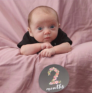 Baby girl posed next to a sign reading 2 months
