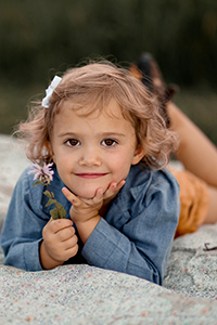 Toddler girl holding flower, laying on blanket with chin in her hand