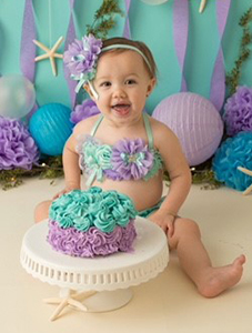 Baby girl dressed as a mermaid, sitting by her first birthday cake