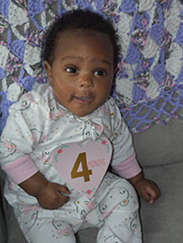 A baby girl wearing a sign that shows she is four months old