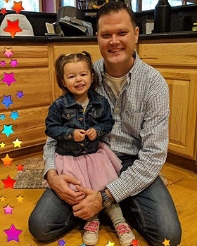 Adoptive dad Greg with his daughter Brooklyn on his lap in their kitchen