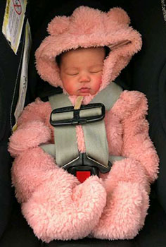 Sleeping baby girl wearing a pink snowsuit, sitting in her carseat