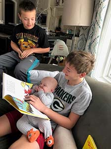 Two brothers reading a book to their baby brother