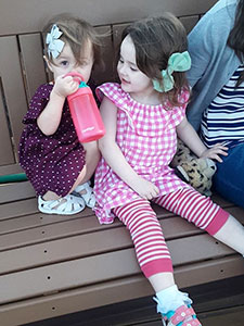 Toddler sisters on a bench with bows in their hair